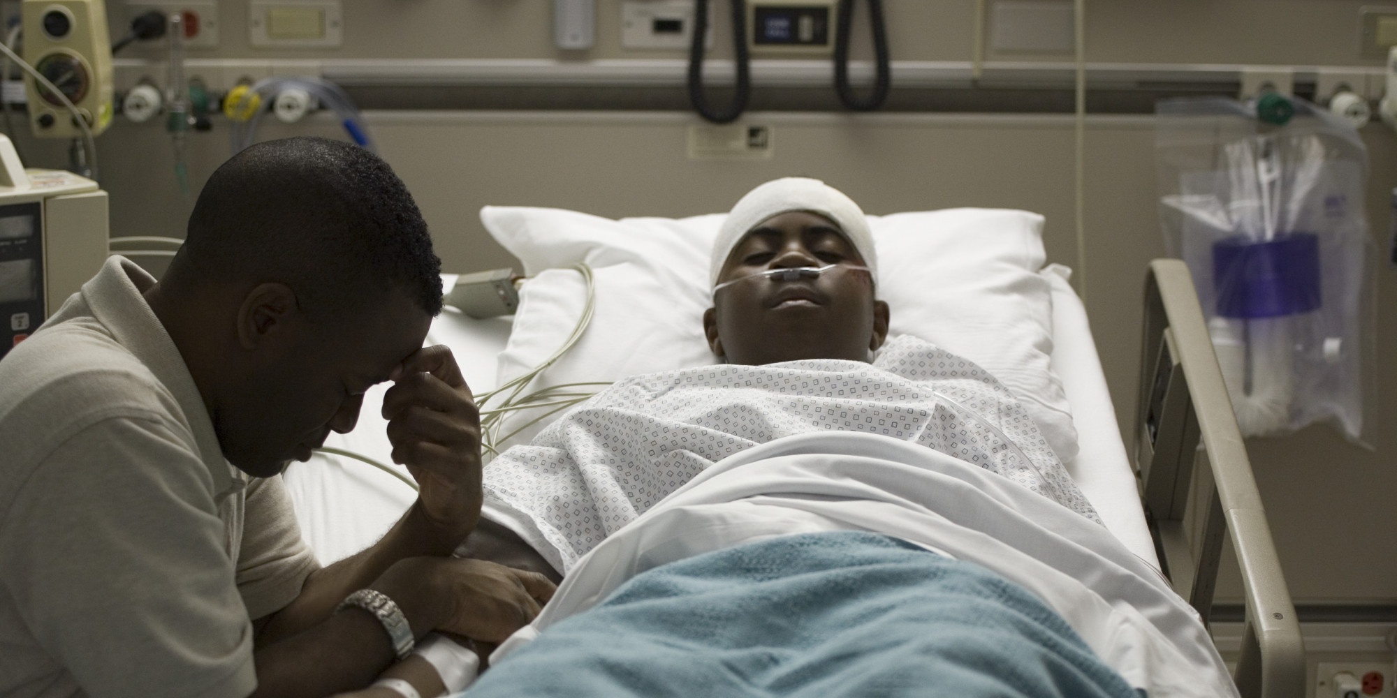 Profile of a father sitting beside his son lying on the bed